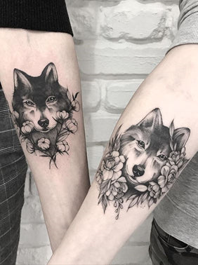 Two forearm black and white wolf tattoos each one surrounded by differing flower arrangements 