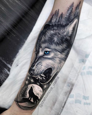 Black and white forearm tattoo of a young wolf with blue eyes looking down at a wolf silhouetted against a full moon and stars
