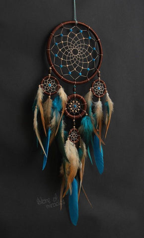 A blue, white and gold 13-point dreamcatcher with feathers and beads attached to a brown ring.
